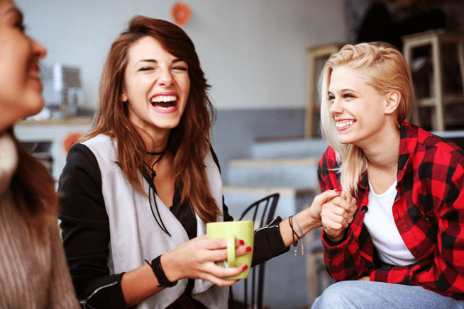 Three women laughing confidently while sitting in a coffee shop.