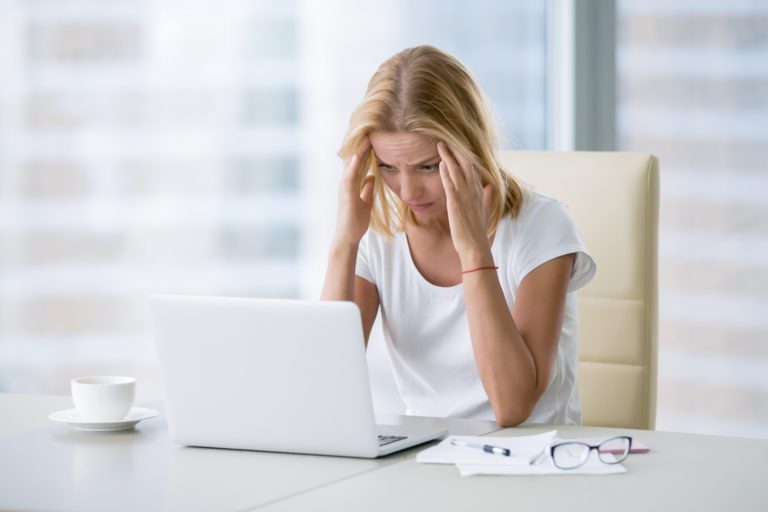 A woman is sitting in front of a laptop, feeling overwhelmed and seeking stress therapy assistance.