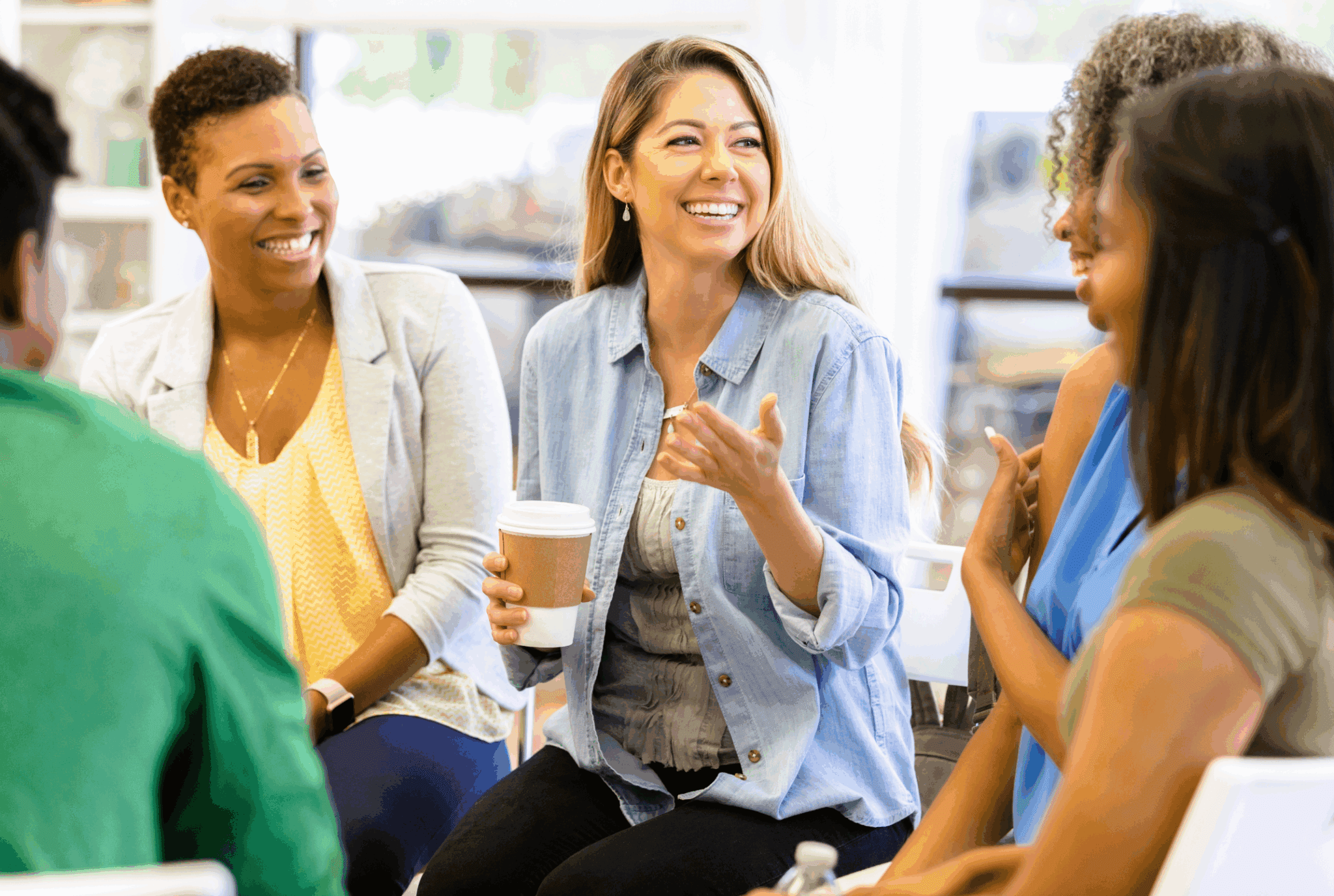 A stock image. The photo shows 3 woman, who are in a casual setting talking. They are different ages and ethnicities. The seem to be sat in a coffee shop. One person smiles to the other two